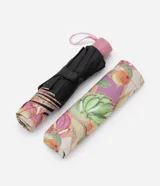 Paraguas plegable de aluminio con estampado de bananas, naranjas y melones sobre fondo lila. Incluye correa de mano y funda protectora.