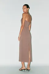 Vestido midi marrón de tejido de punto con escote recto y hombros descubiertos. Presenta detalle de collar metálico con aplicación de joyas, forro interior, bajo con abertura en la espalda, frunces en el tejido y cierre con cremallera oculta en la costura.