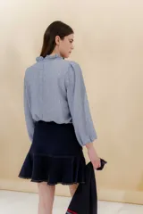 Blusa color beige con cuello mao con volantes, manga larga con puño elástico y cierre frontal con botones ocultos.