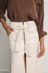 Falda midi color marfil de cuerina, con cierre metálico frontal, cinturón con lazo y abertura delantera.