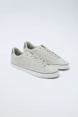 Zapatillas acordonadas de cuero sintético color gris claro, con suela blanca y detalles en gris oscuro en el talón y en la línea superior de la suela.