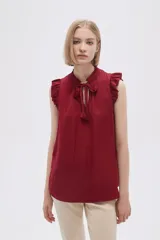 Blusa sin mangas color crudo con cuello con lazo y volados en los hombros.