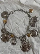 Collar plateado con cadena de eslabones y dijes colgantes de diferentes formas y tamaños, algunos con detalles dorados.