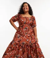 Vestido corto color ladrillo con estampado de flores y palmeras en tonos blanco y negro. Tiene escote cuadrado, mangas cortas abullonadas y falda con volantes.