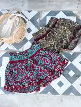 Short de seda con elástico fruncido en la cintura y volado en el ruedo. Presenta un estampado vibrante en tonos rojo/bordó y turquesa con motivos florales o arabescos.