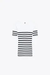 Camiseta de rib a rayas horizontales blancas y negras, de corte ajustado, cuello redondo y manga corta. Presenta un broche metálico en el frente y una medalla con el logo de Zara en la espalda.
