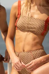 Bombacha de bikini de tiro alto, estilo semivedetina, con estampado geométrico en tonos marrones y beige, y tiras laterales color naranja.