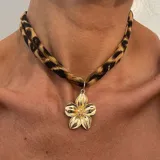 Collar tipo choker con cinta trenzada con estampado de leopardo y un dije grande de cruz dorada con textura martillada.