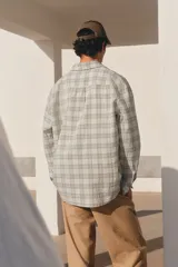 Camisa blanca con diseño a cuadros grises, de corte holgado, manga larga y cuello inglés.