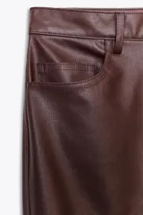 Pantalón negro de tiro medio, con trabillas en la cintura, cinco bolsillos y pernera ancha. Cierre frontal con cremallera, botón oculto y gancho metálico.