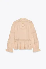 Camisa color crema de algodón con cuello alto, manga larga con puños con volantes y bordados a tono.