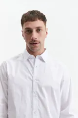 Camisa blanca de manga larga con cuello clásico, cartera abotonada, logo bordado y fit slim. Confeccionada en 98% algodón y 2% spandex.
