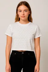 Remera blanca de corte cropped con cuello redondo y mangas cortas. Presenta pequeños apliques metálicos plateados distribuidos por toda la prenda.