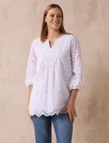 Blusa blanca de algodón con bordado broderie, cuello a la base con escote en V y mangas tres cuartos amplias con puño elastizado.