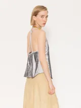 Top corto plateado con breteles finos y espalda descubierta con flecos cruzados.