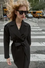 Gabardina larga color beige, con cuello solapa, manga larga con trabillas en hombros y cierre frontal cruzado con botones negros. Incluye cinturón a tono anudado.