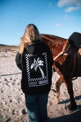 Buzo hoodie negro con capucha y cordón ajustable. Estampado en la espalda con un diseño de palmera dentro de un marco a cuadros.