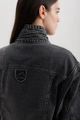Campera tipo bomber de jean negro con cierre frontal dorado, bolsillos laterales y cuello alto. Tiene mangas largas con puños elastizados y detalles de costuras a contratono en cuello y pretina.