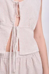 Top sin mangas color crudo con rayas verticales finas en color beige, escote en V con lazos ajustables y corte crop.