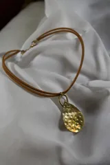 Collar con cordón de cuero sintético color beige y dije de bronce martillado en forma de lágrima.
