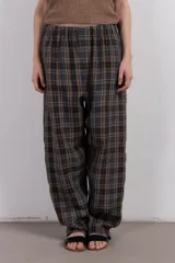 Pantalón largo de corte amplio con estampa escocesa en tonos grises, marrones y blancos. Tiene cintura elástica y tejido suave al tacto.