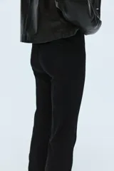 Jean de denim negro con leve stretch, corte ajustado de cintura a cadera y acampanado desde la rodilla al bajo. Es de tiro alto con cierre, botón oculto y corchete. Tiene bolsillos traseros decorativos y pliegues delanteros y traseros.