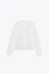 Camisa blanca de cuello subido y manga larga, con detalle de entredós combinados a tono y cierre frontal con botones.