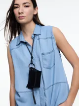 Camisa sin mangas en denim color celeste, confeccionada en 100% lyocell. De corte recto y largo medio, presenta cartera escondida en el frente y un bolsillo plaqué en el pecho. En la espalda, tiene botones decorativos alineados en abertura vertical y pespuntes a contratono.