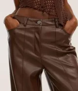 Pantalón de cuero sintético color marrón, de corte recto, con trabillas en la cintura, bolsillos delanteros y traseros, y abertura en el ruedo.