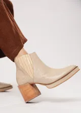 Botín de cuero color beige con textura reptil, elástico lateral y cierre interno. Tiene plataforma delantera y taco de madera.