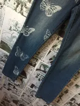 Pantalón de jean azul con estampado de mariposas blancas.
