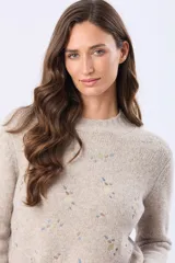 Buzo tejido de abrigo color beige, con cuello redondo y mangas largas. Presenta un delicado diseño bordado en el frente con pequeños motivos en tonos pastel.