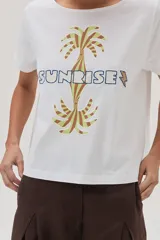 Remera blanca de algodón con estampa de palmeras y la palabra "Sunrise" en el frente.