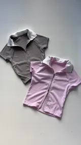 Remera de punto acanalado, color rosa, con cuello polo blanco y cierre frontal con cremallera metálica.