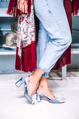 Zapato de tacón celeste con textura tejida, tira trasera y aplique de flor blanca en la punta.