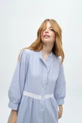 Vestido camisero midi color beige a rayas verticales, con cuello mao, mangas 3/4 abullonadas y festones de algodón en el cuerpo. Cierre frontal con botones.