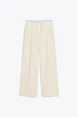 Pantalón de tiro alto color crema, con cintura combinada a contraste tipo boxer con cordones ajustables. Detalle de pinzas en delantero, bolsillos laterales y falso bolsillo de vivo en espalda.