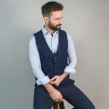 Chaleco de vestir marrón claro con textura de espiga, cuello en V, cierre frontal con botones y bolsillos ribeteados.