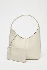 Bolso tipo saca de cuero color gris claro con textura granulada. Tiene asa de hombro y cierre con imán. Incluye cartera interior extraíble con bolsillo.