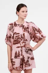 Camisa rosa con estampado de paisaje agreste con pinos, árboles y leones. Confeccionada en mezcla de algodón y lino, con mangas abullonadas y cierre frontal con botones.