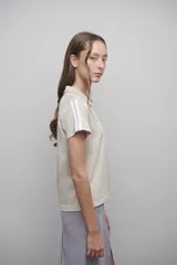 Camiseta confeccionada en remería de algodón, color beige, con cuello tipo polo y escote en V. Presenta dos líneas aplicadas en los laterales de cada manga.