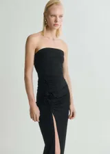 Vestido largo negro sin mangas, con escote strapless, detalle de flores 3D en la cintura, abertura lateral en la falda y corte ajustado.