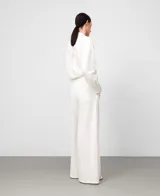 Pantalón blanco de pierna ancha y recta, estilo pareo, con cruce frontal envolvente y cintura elástica en la espalda. Presenta bolsillos laterales y falsos bolsillos traseros.