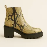 Bota de caña media con estampado de serpiente en tonos dorados y negros, cierre lateral y tiradores en la parte superior. Suela gruesa y robusta con tacón bajo.