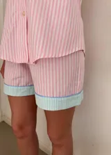 Conjunto de pijama de algodón a rayas verticales rosas y blancas, con detalles en celeste. Incluye camisa de manga corta con botones y bolsillo en el pecho, y shorts con cintura elástica.