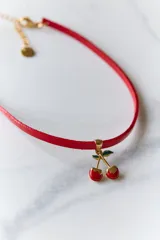 Gargantilla con cordón rojo y dije de cerezas rojas con detalles dorados y hojas verdes.