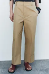 Pantalón color beige de corte ancho, con tiro medio, trabillas en la cintura y raya planchada.