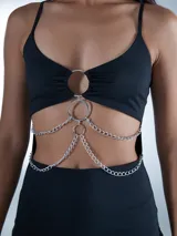 Minivestido negro con breteles finos, escote recto y falda ajustada. Presenta aberturas en la cintura unidas por cadenas plateadas.