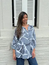 Camisa celeste con estampado batik en tonos grises y blancos, cuello mao con botones y mangas 3/4 con trabilla.