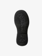 Bota de media caña color negro, con diseño de suela gruesa y estriada. Presenta una correa con hebilla en la parte superior de la caña y un logo de la marca "Camper" en una etiqueta.